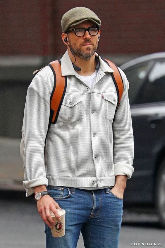 Image of actor Ryan Reynolds sporting his signature casual daytime style, donning a stylish cap, a simple tee, an uncomplicated jacket, and tailored trousers.